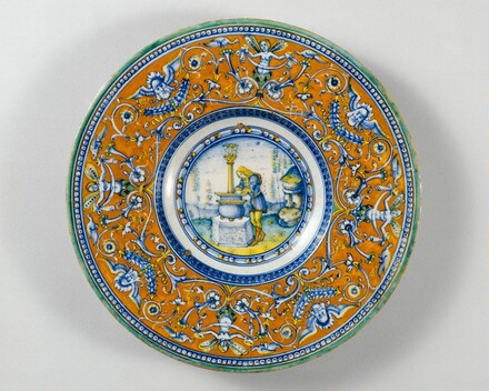 Plate with border of grotesques on an orange ground; in the center, Narcissus gazing at his reflection in a fountain