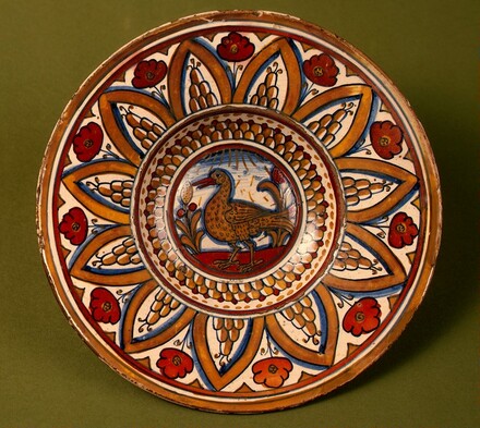 Plate with border of rounded hills within pointed arches with flowers between them; in the center, a wading bird between stylized plants