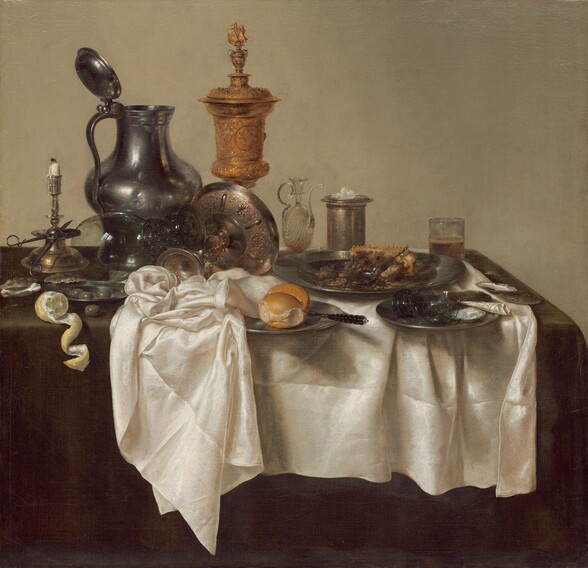A jumble of pewter plates and a pitcher, glass goblets, a gold chalice, a brass candlestick, and other vessels along with lemons, olives, and the remains of a mince pie are arranged on a creamy white tablecloth bunched on a dark evergreen tabletop in this square still life painting. The scene is painted almost entirely in shades of cool grays, gold, brown, and white against a deep beige background. The objects span width of the canvas across its center. At the left edge of the painting, a vibrant yellow lemon has been cut so its rind curls in a spiral that hangs over the front edge of the table. Behind the lemon, a scissor-like candle snuffer is propped against the wide ledge of the tall brass candlestick, its white candle nearly burned down. A few glistening olives sit in a small pewter plate and one olive sits on the tabletop near the lemon and candlestick. A glass goblet with a wide stem with textured knubs rests upended on an elaborately chased, gold, footed vessel that has been tipped over so its wide shallow bowl faces away from us. The tall pewter pitcher behind this is dented on its rounded body. The lidded gold chalice next to the jug is the tallest object in the painting. Next to the chalice, along the right half of the painting, is a glass oil cruet with a long, curving spout, a tall, cylindrical vessel holding a small pile of salt, and a straight-sided, low glass holding beer. In front of these objects, an untouched bread roll and knife sit on a pewter plate at the center of the composition, tucked partially under the rumpled white tablecloth. The remains of the mince pie with its pastry crust on a large pewter plate sits behind another plate holding a broken goblet and a piece of black and white paper rolled into a cone. A few empty oyster shells sit on the table to the left and right, near the lemons and mince pie. The artist signed and dated the painting along the edge of the white cloth near the lower right corner: “HEDA 1635.”