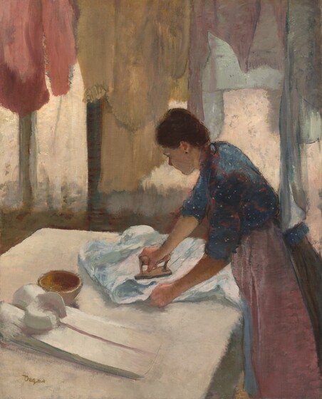 A woman with peachy skin stands facing our left in profile ironing a pale blue shirt on a white surface, possibly a table, with a line of pastel-colored shirts hanging in front of curtained windows opposite us in this vertical painting. We seem to look slightly down onto the woman’s shoulders and onto the surface of the table. The white tabletop takes up most of the bottom half of the composition, and, seen from the knees up, the woman leans in from the lower right corner. The woman’s chestnut-brown hair is pulled up into a bun, and she wears a dark earring in her left ear. Her denim-blue dress is speckled with white dots and highlighted with strokes of blush pink. Her sleeves are rolled up to the elbow, and a dusty rose-pink apron covers her brown skirt. She presses down on the iron with her right hand, farther from us, and uses her left hand to straighten the fabric of the shirt collar. The iron has a thick handle and a flat, narrow, triangular surface used to press out wrinkles. A small, empty, bronze-colored bowl and crisply starched and folded porcelain-white shirt lie on the table to her left, closer to us. A row of hanging garments in pale crepe pink, flaxen gold, teal, and lavender purple soften the light coming into the room from three vertical windows, which are covered with sheer, ivory-white curtains. The artist’s feathery brushstrokes give the painting a hazy quality. The artist signed the work with olive-green letters near the lower left corner: “Degas.”