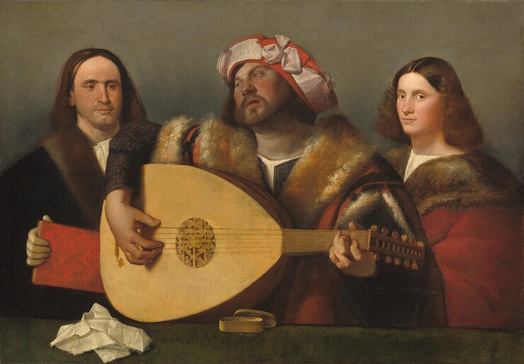 Shown from the waist up behind a forest-green ledge or tabletop, a bearded man with a ruddy complexion strums a six-stringed lute between two, light-skinned people in this horizontal painting. The green ledge runs close to the bottom edge of the canvas, and the people nearly fill the composition. The musician’s body faces us but he looks up and off to our left with gray eyes under arched brows, with lips parted. His long brown hair is covered with a red hat wrapped with a pale, pink band. The ribbon meets in a bow-like form near the front center, and tassels hang to each side. His voluminous coat has wide, burnt-orange fur lapels and is lined with fur where it splits open over his shoulders. The garment below has dark sleeves. He lifts his right shoulder high over the lute as the instrument rests on the tabletop, with the neck to our right. The soundhole at the center is covered with rosette-like tracery. The man to our left has long, straight, dark brown hair and a cleft in his chin, which is darkened with a five o’clock shadow. He looks down and toward the musician with brown eyes over a long nose, and his lips are closed. He wears a black cloak with a fur collar over a white shirt, and holds a red book. To our right, a young person, possibly a man with delicate features, stands with his body angled toward the musician but he turns his face to look at us with gray eyes. He has flushed cheeks, a long, straight nose, and a rounded chin. He has shoulder-length, wavy brown hair parted down the middle, and he wears a red cloak also with a fur lapel, over a cream-white undershirt. A crumpled white cloth and a small, oval-shaped box with its lid askew sits on the green surface near the lute. The background behind the trio is elephant gray.