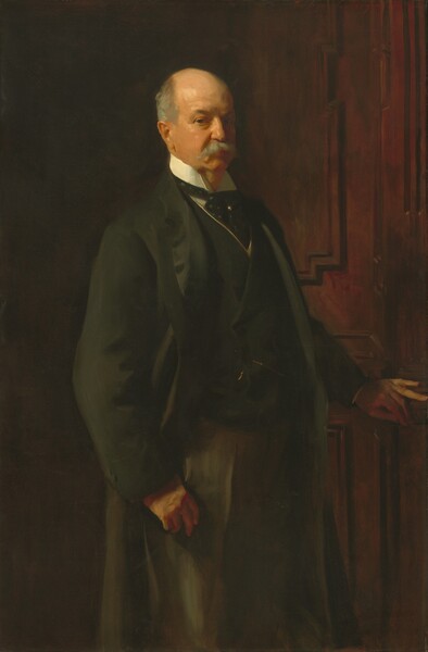 Shown from the knees up, an older, pale-skinned man stands with his body angled to our right as he looks at us from the corners of his eyes in this vertical portrait painting. His short fringe of hair around a balding head and his bushy moustache are steel gray, and he gazes at us with brown eyes under thick brows. A long, hooked nose and small red mouth are set in his jowl-lined face. He wears a long, fern-green coat with a matching vest trimmed in gold over a white shirt. A polka-dotted, pine-green cravat is tied around the standing collar and held in place with a gold pin. Two copper-colored brushstrokes near his waist suggest a pocket watch chain. The hand closer to us hangs by his hip with the thumb hooked into the pocket of his trousers, which are loosely painted with long strokes of olive and sage green. His other hand rests on the mahogany-brown wooden door that fills the space beyond him. Inset panels on the door are outlined in darker brown to create stepped, geometric shapes. The man is warmly lit from the upper left and the background is in shadow. The artist signed and dated the painting in the upper right, “John S. Sargent 1902.”