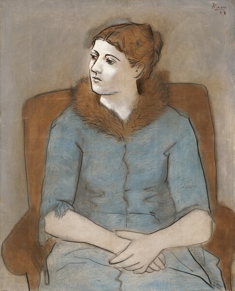 Shown from the knees up, young woman with ivory-white skin sits facing us in a brown armchair with her hands loosely clasped in her lap in this vertical portrait painting. Her hair is parted in the middle and gathered at the back of her head. Her head is turned to our left and she looks off into the distance with dark brown eyes under thin, arched brows. She has a long nose and a pale, petite mouth. Her steel-blue dress has elbow-length sleeves and a brown fur collar. The blue dress is marked with off-white, zigzagging lines and shadows are created with gray smudges. The armchair frames her torso, being just taller than her shoulders and wider than her arms. The chair, her hair, and collar are all ginger brown. Wavy lines and angled strokes of smoke gray and black delineate the texture of her hair, collar, and folds of her dress. Her facial features, clothing, and the chair are outlined in black and set against a taupe background. The artist has signed and dated in the upper right, “Picasso 23.”