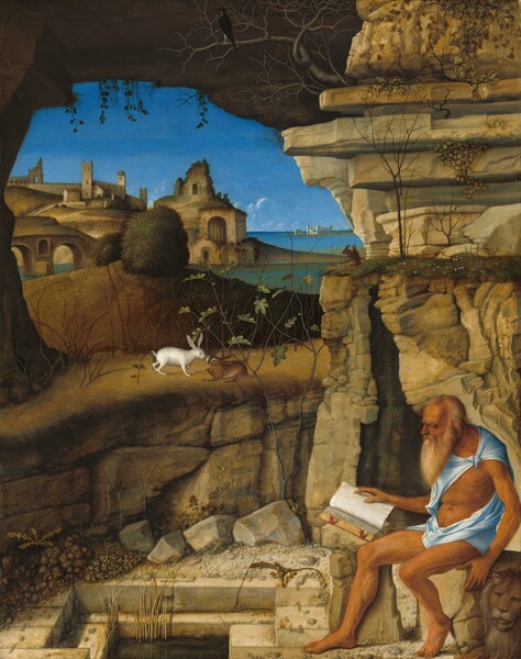 A bearded and balding man with deeply tanned skin, dressed only in a strip of robin’s egg-blue fabric around his shoulders and hips, sits reading a book on a rock at the entrance to a craggy cave, in front of a landscape in this vertical painting. In the lower right corner of the composition, the man, Saint Jerome, faces our left in profile, his head bowed toward the open book propped on the rock near the knee farther from us. His hair and beard are parchment white, and he has a prominent brow ridge, a long, hooked nose, and sunken cheeks. His arms and legs are sinewy and his torso is muscled. The blue cloth is knotted over his left shoulder and wraps around his hips. A lion lies next to Saint Jerome in lower right corner, his face toward us with his mouth open. There is a rectangular pool lined with blocky, cream-white stones at Saint Jerome’s feet, to our left. The cave behind him, to our right, has a jagged, narrow, vertical entrance, and there are rocky outcroppings above and to our left, over the pool. A stone arch spans the top edge of the painting, enclosing the scene below. Other animals appear around Saint Jerome, including a lizard near the pool; a squirrel on the grassy top of the cave entrance; and a black bird in the barren branches of a tree growing from the rocks above the cave. On the far side of the pool, two rabbits, white and brown, touch noses on a grass-topped, low, rocky wall. There is a hill with two dark green bushes beyond that. In the distance, a cluster of tan-colored, stone buildings, some in ruins, spread down a hillside to the water’s edge. Across the water to our right, deep in the distance, white buildings line the horizon, which comes about two-thirds of the way up this painting. A few puffs of white clouds float along the waterline against a vivd, azure-blue sky above.