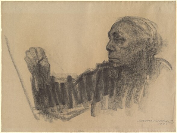 This horizontal drawing shows the head, chest, and one arm of a person in the act of drawing. Created with wide, soft black marks against bone-colored paper, the person faces our left in profile and raises their right hand, farther away from us, close to a diagonal line probably representing paper or another surface. Long hair is pulled back from a high forehead and the person has dark eyebrows, a prominent nose, high cheekbones, and their lips are pulled slightly down at the corners. A dark line between the thumb and forefinger of the raised hand represents the drawing material, held near the diagonal line. The face and hand are more detailed than the body, which is blocked in with vertical, zigzagging lines. The artist signed and dated the work in the lower right corner: “Kathe Kollwitz 1933.”