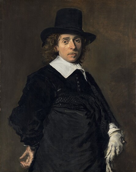 Shown from about the hips up, a man with peachy skin, wearing an ink-black hat and coat with a bright white collar, looks out at us against a dark background in this vertical portrait painting. He stands with his body angled to our right and his face turned to look at us with dark gray eyes. His slim face is framed in long, brown curls under his tall, brimmed hat, which is cocked a little to our right, away from us. He has a straight, prominent nose, lightly flushed cheeks, and a wispy, light brown mustache above a small, pointed goatee under his lower lip. His neck is encased in a broad, starched, white linen collar, its wings lying along his collarbones. His velvety black coat has a row of tightly spaced buttons down the front. A cummerbund or sash wraps around his waist and hips. He rests his right hand, on our left, against his hip near his lower back, palm facing out. He wears a light, dove-gray glove on his opposite hand, and holds a second glove in that hand. The background is earth brown. The portrait is painted loosely, with broader brushstrokes in some areas, such as the hand at his hip and in the folds of the black garments.