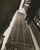 From close to the ground, we look sharply up at three skyscrapers that nearly meet in the empty sky in this black and white photograph. The building in front of us has more than twenty-five stories, each of which is lined with windows. The building to our left is deep in shadow as it zooms steeply into space. Sun warms the top half of the building to our right. Only a sliver of sky is visible between the left and center building, and where the three meet in the deep distance.