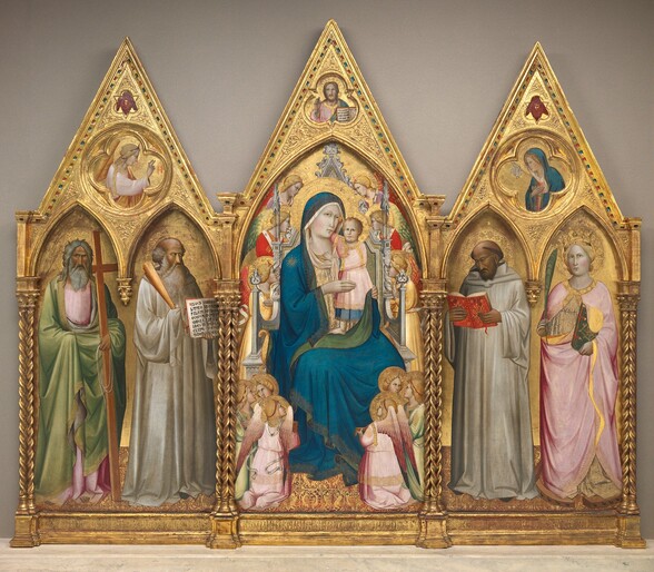 This altarpiece is made up of three panels, with a woman and baby sitting on a throne surrounded by winged angels at the center and flanked by a panel to either side that each shows two people standing under pointed arches. The background across all the panels is gold, and the top of each panel comes to a triangular point above. Spiraling columns frame and separate the sections. The people and angels have pale or deeply tanned skin, and wear robes in silvery-white, pale pink, celery green, crimson red, or pale yellow. They all have plate-like halos, which overlap for some of the angels around the throne. The floor across all three panels is patterned with gold against a burgundy-red background. The central panel shows a woman, Mary, wearing a lapis-blue robe, propping a standing baby up in her lap with both hands. The baby wraps one arm around her neck and grips the neckline of her dress with the other. The twelve angels around them look on from the sides or from small groups in the lower corners. Above the pointed arch over the throne, a bearded man is shown from the chest up in a shape of three lobes alternating with three points. That man faces us and holds up his right hand, to our left, with the first two fingers raised. He holds up an open book with Latin text with his other hand. In the panel to our left, two men with tan skin and gray hair and beards stand with their bodies angled toward the central panel. The man to our left holds a tall wooden cross and the man to our right holds up an open book with Latin text with one hand and a bundle of rods with the other. The gable above has a circle carved into its center. In that roundel is an angel inside a four-lobed quatrefoil, shown from the waist up facing our right. In the right panel, a man with tanned skin and a woman with pale skin stand under pointed arches. The man, to our left, holds and looks down at the pages of an open red book. To our right, the woman holds a palm frond in one hand and a closed green book in the other, and she stands in the circle of a wooden wheel lined with black spikes. The roundel above the pair shows a woman and a dove inside a four-lobed quatrefoil. Inscriptions appear with gold letters against a gold background across the bottom of each panel, so are difficult to make out. The panel to our left reads, “S. ANDREAS AP L U S; S. BENEDICTUS ABBAS.” Under the central panel, text reads, “AVE MARIA GRATIA PNELA DOMINUS.” The third panel reads, “S. BERNARDUS DOCTOR; S. K TERINA VIRGO.” Latin in the two books held outward is also legible. The book in the leftmost panel reads, “AUSCU LTA.O FILI.PR ECEPTA .MAGIS RI.ET.IN CLINA.AUREM CORDIS.T UI A MONITIONE M.PII.PA TRIS.LI BENTE R.EXCIP E.ET.EF.” In the central panel, the Latin inscription reads, “EGO SUM A O PRINCI PIU FINIS EGO SUM VI A. VERITAS VITA.”