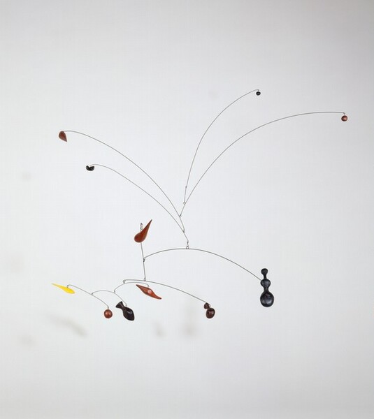 This free-floating sculpture, called a mobile, hangs from a wall or the ceiling. At the top, four wires curve upward in a spray, two to each side. Below, six wires bow in descending branch-like forms. Eleven small shapes, each in the form of a ball, comma, hourglass-like shape, or paddle, is affixed to or hangs from the end of each wire, and each is a single color in black, yellow, or red.