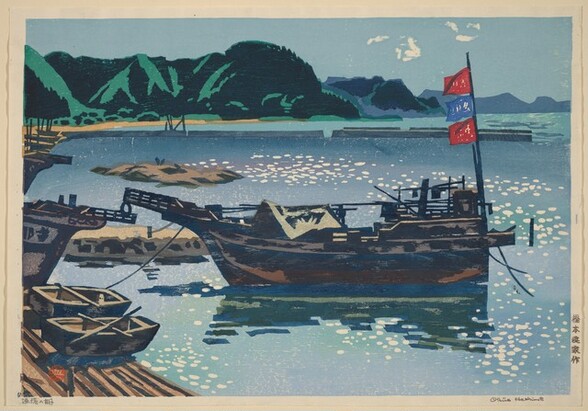 Several rowboats and larger boats are pulled in along a sandy shoreline, surrounded by a body of glimmering, topaz-blue water with emerald-green hills in the background in this horizontal, color woodblock print. Five Japanese characters are written in the margin of the paper near the lower right corner. The name Okiie Hashimoto is written in graphite under the lower right corner of the printed image, and more Japanese characters are written in graphite under the lower left.