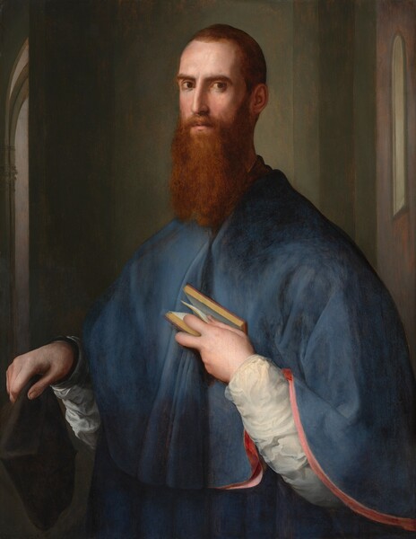 A  light-skinned man with short, auburn-brown hair and a long beard is shown from the hips up, his chest and sloping shoulders covered by a muted cobalt-blue cape in this vertical portrait painting. His body is angled to our left and he looks at us from the corners of his brown eyes under curving, low brows. His head, torso, aquiline nose, and hands are slightly elongated. He holds a black hat in his right hand, on our left, close to his body. His left hand emerges from a white sleeve painted with swirling brushstrokes, as he presses a small book to his chest, holding it open with one page caught between thumb and index finger. The lower edge of his cape drapes over that arm, revealing rose-pink lining. He stands with his back to a grayish-green wall that does not span the width of the composition. Slivers of other spaces, possibly rooms, are suggested by tall, narrow views of windows and arched openings along the sides of the painting.