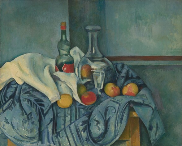 A glass bottle, a glass carafe, a stemmed glass, several pieces of fruit, and white and blue cloths are arranged on a wooden table in this horizontal still life. The bottle and carafe are at the center of this composition. The bottle has a crimson-red label, and the carafe has a tall, narrow neck and a rounded body. The stemmed glass has straight, flaring sides, and it sits on the table just in front of the carafe. Several pieces of fruit, painted in reds and yellows, are interspersed on the white cloth that surrounds the glassware. The muted, celestial-blue tablecloth is patterned with scrolls and leaves, and it bunches around the objects on the tabletop. The wall behind the table is mottled with cool blues and greens, and a brown line, perhaps a chair rail, runs from behind the still life to the right edge of the painting. Short brushstrokes are visible throughout.