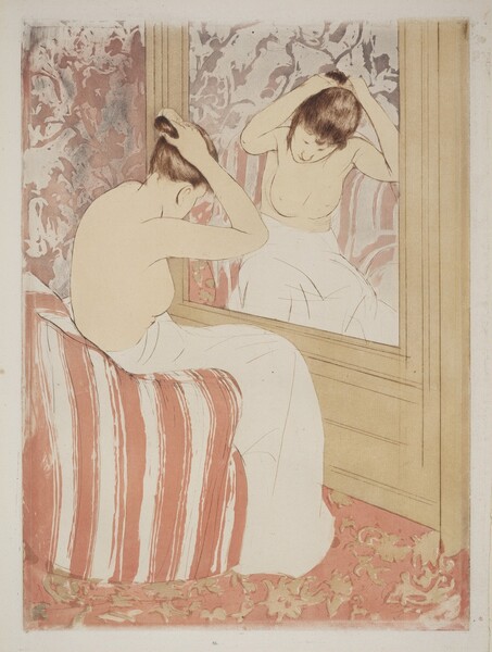 A pale-skinned woman, nude from the waist up, gathers her hair in her raised hands as she sits before a mirror in this vertical, colored print. The large mirror is to our right, and the woman’s body is mostly turned away from us. Her head is bowed but a loose tendril of brown hair hanging beside one cheek is reflected in the mirror. Her lower body is wrapped in a voluminous off-white cloth as she leans forward on a curved terracotta-red and white striped armchair. Her facial features, the contours of her body, and the folds of the towel are all delineated with thin strokes of tawny brown. The mirror is set into a tan wall, and the wall beyond and carpet below her covered with abstract floral patterns. The wall has a dusty-rose motif over an off-white background with washes of light gray while the carpet pattern is tan over a peach background. The wall and chair are reflected in the mirror in paler tones.