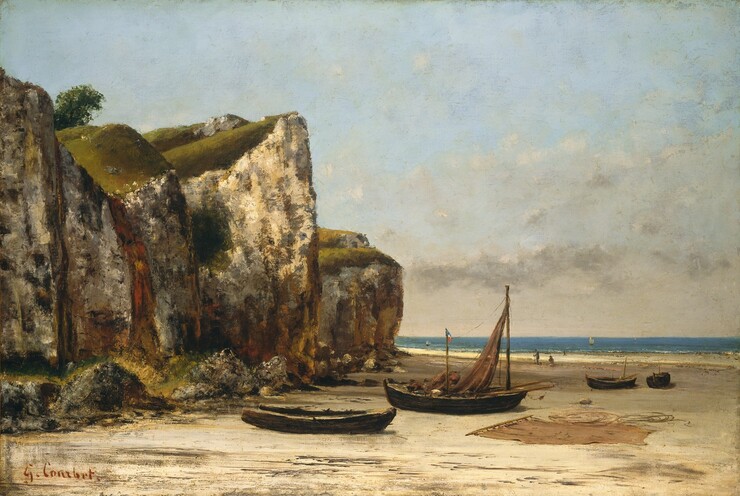 Towering, sheer cliffs loom to our left, over a sunny beach scattered with boats in this horizontal landscape painting. The chalky, rugged faces of the cliffs are dappled and streaked with olive green, dark brown, gray, rust red, and mustard yellow. The horizon comes a third of the way up the composition so the cliffs are outlined against the powder-blue sky, which is loosely veiled with wispy, cream-white clouds. The mossy tops of the cliffs are illuminated by sunlight from the upper left, and a solitary leafy tree leans into view between the two cliff-tops closest to us. Four empty, wooden boats sit on the flat, sandy beach below. We look onto the long sides of the two closest to us. One is stripped and appears dilapidated, while the one behind it has a ginger-brown sail attached to the mast in the prow. Two more wooden poles or oars jut out from the cockpit on either side of the mast. A small flag with horizontal bands of blue, white, and red flies from a short pole near the middle of the boat. A bundle the same color as the unfurled sail sits in the boat. Another sail is spread out on the sand to our right, and coiled ropes lie nearby. The two other boats are slightly further back on the right, with one angled to our left while we view the other straight on. There are two people a short distance beyond these boats. One faces our left in profile while the other sits on the sand looking toward the water. Thin trails of white delineate the low surf and a few sailboats drift by on the brilliant blue water. The artist signed the lower left, “G. Courbet.”