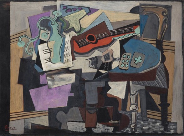 Abstracted objects, including a guitar, vase, papers, and playing cards, are gathered on a tabletop in this horizontal still life painting. The objects are made up of areas of mostly flat color and many are outlined in black, creating the impression that the some shapes are two-dimensional and assembled almost like a collage. The brown table has an oval top and a curving pedestal foot. At the center of the jumble on the tabletop, a guitar lies on its side with the neck facing us and reaching to our right. Beneath the black fretboard and neck, the curving form of the guitar is painted tomato red. The upper half is represented by a squared-off brown form. The guitar seems to rest atop or in front of an array of stacked shapes, like splayed pieces of paper, in white, lavender purple, and pale blue. A curving form painted in turquoise to our left seems to be a vase holding a spray of three flowers. The vase is shown against a white square painted with horizontal black lines, like sheet music. A dark gray form at the middle of the table, beneath the guitar, could be the silhouette of a bird facing our left. Just to the right of the bird, a pair of playing cards lie on a blue area. Painted in turquoise against gray, one card has six dots and the other one club. A chair with a curved, arching top and a gray upholstered seat is pulled up to the table to our right. The front left leg is light gray with turned knobs near the foot and halfway up the leg; the right leg is painted black, as if in shadow. Panels of pale tan suggest wainscotting behind the table beneath a pale gray wall across the background. The overall impression of the painting is fragmented as even single objects seem to be broken up into planes and areas of color. The artist signed and underlined his name with red paint in the lower left corner: “Picasso.”