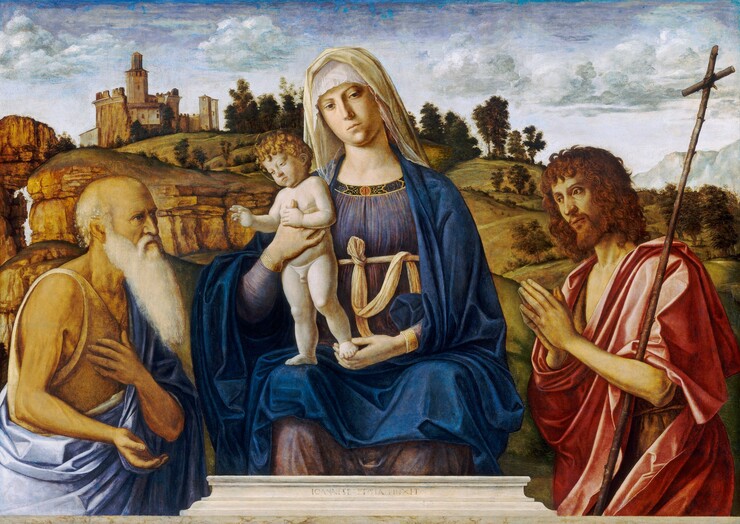 A woman holding a baby, who stands on her lap, is flanked by two men in a deep landscape in this horizontal painting. At the center of the composition, the woman sits behind a stone ledge. Her pale-skinned, oval face tips to our left, and she looks down and to our right with brown eyes. She has a long, straight nose, round cheeks, a slight double chin, and her pale lips are closed. A white cloth drapes over a translucent veil that covers her forehead. Her indigo-colored dress is edged with gold writing and ornamental designs against a red and black background. A parchment-brown cloth is tied as a belt under her bust. The nude child with notably pale skin stands on one of her knees, and she holds his other foot with one hand. Her other hand braces his chest, and he holds onto that thumb. His other hand is held up with the thumb and first two fingers raised toward the man to our left, at whom he looks. A halo, drawn as a thin gold line, encircles his blond curls. He has chubby cheeks and thighs but looks seriously at the man to our left. Both men have tanned skin, and they face inward, almost in profile. They are shown from about the hips up on the far side of the stone ledge. The man to our left is balding with a long, white beard. Wrinkles line his forehead and cheeks. He looks off to our right with shadowed eyes, and he has a hooked nose. He wears a tan garment under an ultramarine-blue cloak, which drops from one shoulder and wraps around his hips. He holds one hand to his chest and the other palm up. To our right, the second man looks to our left with deep-set eyes. He has high cheekbones, a straight nose, and his lips are parted. Copper-brown hair falls in shaggy curls to his shoulders, and he has a full, red beard. His hands are together in prayer in front of his chest, and a tall thin stick with a narrow crossbeam to make a cross is tucked into one elbow. His voluminous, carnation-pink robe almost covers a brown, shaggy garment beneath. Beyond the group, rocky cliffs lead back to a castle-like structure to our left and grassy, tree-dotted hills roll into the distance to our right. Pale gray and white clouds drift across a violet-purple and blue-streaked sky across the top quarter of the composition. The artist signed the work as if he had carved into the stone ledge in front of Mary: “IOANNES BAPTISTA PINXIT.”