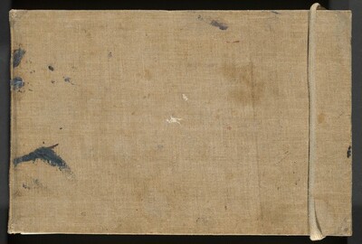 This tan-colored, fabric-covered sketchbook cover is marked with a few smudges of dark gray and white paint. The binding is to the left in this photograph. The cover is wide and has a cream-colored rope wrapped around the narrower end to our right. The weave of the fabric is visible. A few swipes of gray paint are spaced along the binding, to our left, and there are tiny touches of white, lavender purple, and brick red marking the cover.