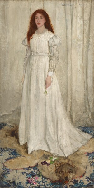 A young woman with pale white skin, wearing a long, flowing white dress, stands in front of a white curtain in this full-length, vertical portrait. Her red hair cascades down over and behind her shoulders. She looks to our left with green eyes, her pink, full lips closed. Her dress has puffed shoulders above a white-on-white striped pattern on the long sleeves. She stands on an animal pelt; it is not clear whether it is a wolf or a bear. The pelt spans the width of the painting and overlaps a blue patterned carpet. The animal’s mouth gapes to show sharp teeth and its glassy eyes are wide open—and it seems to look at us. The woman holds a white lily by her side in her left hand, while yellow and purple pansies lie scattered on the pelt.