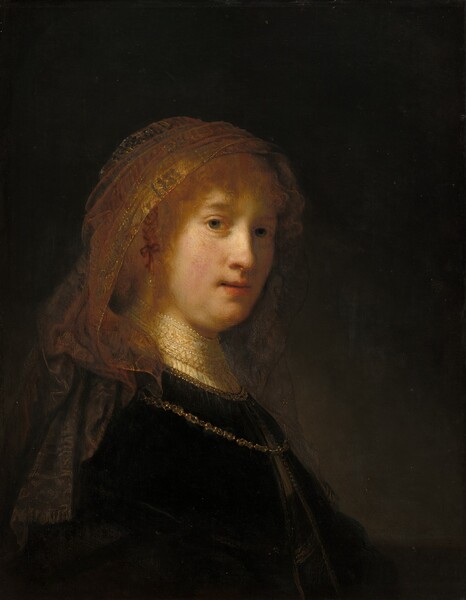 The face of a young woman with pale, peachy skin materializes from a deeply shadowed background in this vertical portrait painting. Shown from the waist up, her body is angled to our right, and her face turns to look at us. She has gray eyes, a rounded nose, and her pink lips are slightly parted. A golden veil covers long strawberry-blond hair and falls down over the shoulders of her dark dress. The dress has a high, white lace collar, and a gold chain hangs over her shoulders and on her chest. Painted mostly with deep browns and earth tones, the light that falls on her face and hair creates an aura-like effect.