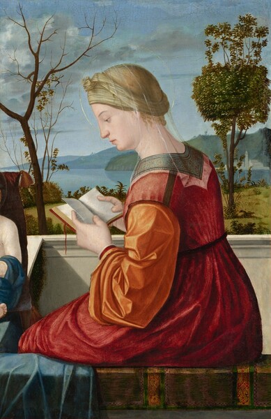 Shown from the hips up against a landscape, a woman with pale skin, wearing a burgundy-red dress with marigold-orange sleeves and a sheer veil, sits facing our left in profile as she reads a small book in this vertical painting. She has a straight nose and peach-colored lips. Her blond hair is covered by a bone-white headdress tied over her forehead. The veil drapes over the headdress, and her head is encircled with a faint gold ring, creating a halo. Her dress has full sleeves and is cinched into pleats at the high waist. The neckline is edged with a band of nickel gray decorated with a pattern of circles and leafy forms. The book has a red cover with a red ribbon, and she holds one index finger between the pages. A low chalk-white stone wall beyond the woman suggests she sits on a porch or balcony. A swath of powder-blue fabric drapes over the ledge on which she sits near one knee. To our left, a sliver of a shoulder, elbow, and toes of one foot suggest a person with pale skin draped in midnight blue, leaning back against a maroon-red pillow with tassels at the corners, in front of the woman and to our left. Behind that second person, in the landscape beyond the balcony, barren branches of a tree twist against the sky while a second tree, to our right, has a leafy, green canopy. A mustard-yellow meadow lined with bushes leads to the water’s edge, where ice-blue water leads back to rolling hills along the horizon. A few white buildings and a tower are clustered on the opposite shore. White and gray clouds float against the pale blue sky.