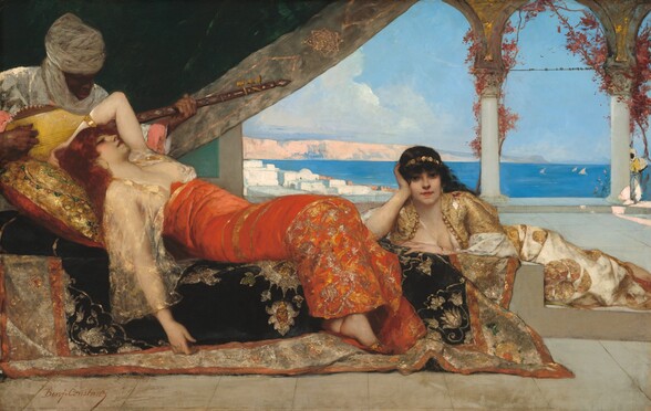 This horizontal painting shows a daylit, covered terrace, where two women with pale skin and wearing long dresses lounge and recline along a ledge as a turbaned man with dark brown skin plays a musical instrument. To our left, behind one of the women, the musician's white turban drapes around his neck. His white shirt has wide, salmon-pink cuffs. His head is bent over a stringed instrument with a light yellow rounded body and a long, narrow wooden neck. His features are mostly lost in shadow but his closed lips are dark pink. Behind and framing the musician, a dark green drapery with gold edging cuts across the top left corner of the painting and is drawn back to reveal a bright sea view beyond. Close to us, one woman wears an orange-red dress with gold embroidery and a low-cut transparent blouse that shows her pale skin beneath. She lounges on her back, head near the musician, and body splayed along the ledge out toward our right. Her eyes are half-closed, and her head rests on a large gold pillow with green and pink embroidery over which her long, dark red hair cascades. Her left arm is bent and thrown back behind her head while her right arm hangs limply toward the floor. Her extended legs are bent, and feet with red and gold pointed slippers emerge from the bottom of the dress. Beyond her legs and to our right, the second woman reclines in a gold and cream-white dress with a filmy top and gold jacket. She rests her head in her hand, propped up by a crooked elbow resting on the ledge, while her body extends to our right. She gazes at us with dark eyes. She has dark brown, wavy hair that flows behind her shoulders, and she wears a gold headband with round, coin-like links. Beyond the group of three, another man stands to the far right in the background, in a corner of the terrace patio next to a pillar. Like the other man, he has dark brown skin and wears a turban, a loose white shirt under a yellow vest, and light blue, loose trousers. The back of the terrace opens to a bright and sunny day, the light blue sky scattered with thin white clouds above a vivid blue sea, where three sailboats approach the port. Distant mountains are bathed in light and appear pink, beyond the white roofs of the port or village along the water's edge, to our left.