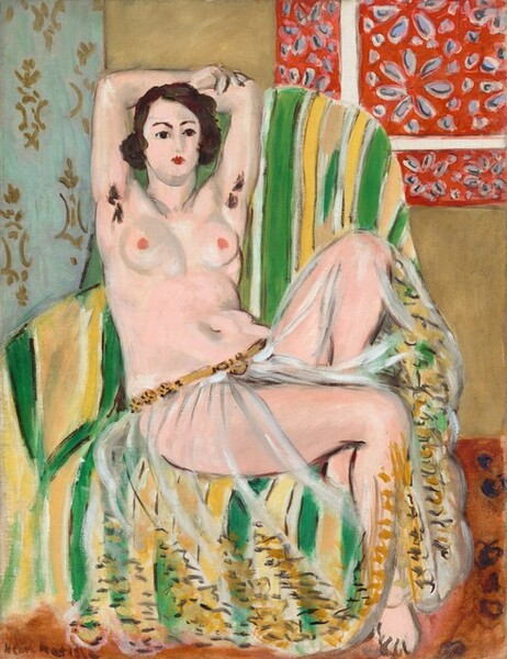 A nearly nude woman with a pale, pink complexion leans back into a striped, upholstered chair with her arms overhead, holding opposite elbows, and one foot tucked under her in this stylized, vertical painting. The scene is painted loosely, making some details indistinct. The woman’s torso faces us but her legs are angled slightly to our right, and she looks off in that direction with dark brown eyes under dark, arched brows. Her features are loosely painted but she seems to have a straight nose and her small, scarlet-red mouth is closed. Her dark brown hair curls down to her ears in a chin-length bob. She wears only a gauzy, transparent cloth, which is gathered low on her hips with a golden-brown belt. Loosely painted, short and zigzag strokes of chocolate brown and harvest gold suggest a wide band of embroidery or decoration around the bottom hem. The woman’s raised arms show two tufts of dark brown hair in her armpits. She has round breasts with dark pink nipples, and a curving belly and hips. Her left knee, farther from us, is bent sharply against the back of the chair so her foot is tucked behind her other thigh. The chair is striped with lime green, white, and lemon yellow. The floor is terracotta orange. A strip of light blue with a gold pattern to the left and a red area with a flower pattern to our right suggest fabrics draped on the sand-brown wall. The artist signed the work in the lower left corner, Henri Matisse.
