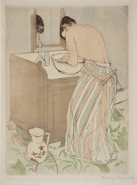 A pale-skinned woman bends over a basin of water on a washstand in this vertical, colored print. The woman is angled away from us so only her ear and the curve of her forehead are visible beyond her hunched shoulder. Her upper body is bare, her dress having been unfastened so it hangs around her waist. The dress is striped with frosty green, shell pink, and the cream white of the paper. Light gleams on her dark brown hair, which is tied up and back. She cups her hands in the light blue water of the white basin. Two bottles sit at the back corner of the washstand, and a mirror reflects the top of her head. The fawn-brown washstand is boxy, and a handled white pitcher painted with muted pink flowers is at the front left corner, which is closest to us. The wall beyond the washstand is pale, arctic blue, as is the carpet, which is also patterned with pea -green leaves. The artist signed the work in graphite under the lower right corner, “Mary Cassatt.”