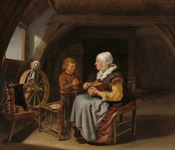 Lit brightly against an otherwise shadowy room, a seated, older woman and a standing young boy face each near a spinning wheel in this horizontal painting. Both have pale skin. The woman sits in a wooden chair facing our left in profile, as she cuts a slice into the top of a brown loaf in her lap. Her eyes and downturned mouth are lined with wrinkles, and jowls sag along her jawline. She has slightly protruding eyes, and the skin of her neck hangs a little loose. Her head is wrapped in a white, lace-edged scarf, which is gathered at the base of her skull. She wears a white, pleated ruff around her neck, which rests across a brown vest over golden-yellow sleeves. Light shimmers on her slate-gray apron, which drapes over a muted, cinnamon-brown skirt. The toes of black shoes peek out beneath her skirt, propped up on a block. She looks toward the boy who stands at her far knee, to our left. His body is angled toward the woman so his face is in shadow, and he looks down over clasped hands. His fingers are interlaced except for his steepled index fingers. He wears a worn brown jacket with frayed cuffs, and silver buttons down the front. His pants are olive green and his shoes are brown. A plate with a yellow substance sits on a three-legged stool near the woman and boy. Next to it, near the wall to our left, sunlight coming in from that window glints off the wooden spinning wheel. A handful of unspun, white wool sits in a cage atop a staff resting through the spokes of the wheel. Wood beams run across the wooden ceiling and frame the walls. The floor is also wood.