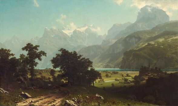 From a little above a dirt road, we look past a grove of trees to a broad plain and a lake at the foot of towering, hazy mountains in this horizontal landscape painting. The narrow, teal-blue lake runs from left to right along the horizon, which comes about a third of the way up the composition so the hills and mountains take up most of the picture. On the far shore of the lake, steep hills are thick with fern-green trees and growth. Beyond these hills, muted gray and green rocky mountains reach precipitously into the clear, robin’s egg-blue sky so some nearly touch the top edge of the canvas. Snow nestles in the mountain peaks while gauzy mist hovers among the mountain tops. The meadow below is a patchwork of avocado-green and sand-brown fields. An ice-blue stream winds from the lake across the plain while olive-green trees and shrubs dot the fields. Closest to us, in the lower left corner of the painting, small stones and clumps of green grass run along the dirt road, and boulders line it to either side. A band of dark green spanning the road creates a screen a short distance from us, in the lower left quadrant of the composition. Through the trees is a view of miniscule buildings lining the lakeside. In the shadows, under the trees, people camp with a covered wagon covered in white fabric and several animals including a donkey. A red and yellow fire glows, almost lost in the deep shadows of the trees, next to the people. On our right, about a dozen people with a horse-drawn wagon, all tiny in scale, work in the field next to the stream. Farther along the stream, another wagon approaches a covered bridge. On our right and close to us, a dark shadow falls across the landscape. Beyond the shadow, a group of buildings with a church in the center sit on a low hill.