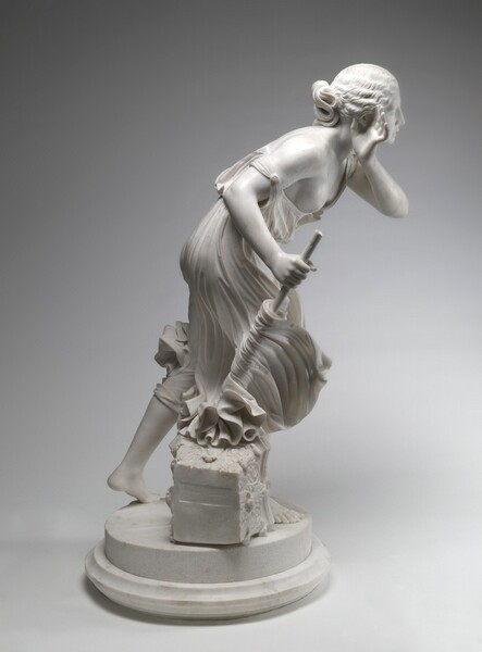 Carved from white marble, a girl steps and leans forward on a disk-like pedestal with a wide fluted base in this free-standing sculpture. In this photograph, she steps away from us to our right. She wears a flowing, knee-length dress or toga, which swirls around her, and her feet are bare. She leans forward at the hip, with her bent right leg supporting her weight. Her other leg extends behind her, toe tapping the base with her heel lifted, as if mid-stride. She holds her left hand up to cup her opposite ear, with her elbow lifted as she leans forward. Her right hand clutches a staff, arm bent at the elbow, which she thrusts downward. The end of the staff meets a fragment of a column at her foot, about the height of the girl’s shin. The capital is carved with decorative leaves and shell-shaped designs. The skirt flickers around the stick as if in a strong wind. The right side of the dress has dropped off her shoulder, baring one breast. The exposed body and limbs are round and smooth. Her hair, carved in undulating waves, is loosely swept back, with a cascade of waves falling over her left shoulder. Her face is round and full, and her expression concentrated, with a furrow in her brow and her mouth turned downward, eyes closed. The column fragment at her feet has one smooth face, which is incised with a rectangle carved with the name “Randolph Rogers” and the date, “1860.”