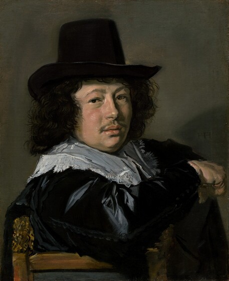 Shown from the chest up, a young man with a plump, pale-skinned face hooks one elbow over the back of a wooden chair and looks at us in this vertical portrait painting. The man’s body faces our right as he turns his head over his right shoulder, closer to us, to gaze out with brown eyes under lifted brows. His nose ends with a round bump, and his round cheeks are flushed. He has a wispy mustache over full pink lips, which are parted. He wears a tall-crowned, brimmed black hat over a cloud of wavy, shoulder-length black hair. A lace-edged white collar spreads over an ink-black, satin coat. His right elbow is planted across the back of the chair, which has carved finials to either side. That hand is closed in a fist, which may hold something. The man’s hat casts a shadow on the right side of the taupe-gray wall behind him, where the artist has signed the painting with two monograms of his initials, “HF.” The brushwork is loose throughout, especially so in the man’s clothing.