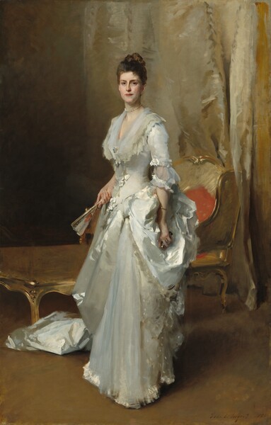 A woman with pale, peachy skin and dark brown hair, wearing a long sleeved, floor-length white satin dress, stands facing and looking out at us in a room hung with shimmering, ivory-white drapery in this vertical portrait. The woman’s body is angled slightly to our left and her hair is piled on top of her head. She has dark eyes, a straight nose, and her rose-red lips are closed. She wears pearl earrings, a string of pearls at her throat, and a brooch with two large pearls at her chest. The deep V-neck of her dress is edged with layers of sheer fabric that drapes over her shoulders. Some areas of the dress are loosely painted but gives the impression of lace edging along the collar and bows down the front of the bodice and at the elbows of the half sleeves. The train of the dress bunches around her feet behind her to our left and is either gathered at her left hip, on our right, or her dress has a voluminous bustle there. She holds a partially open fan in her right hand, on our left, and black opera glasses in the other hand, nestled into the bustle. She wears a gold bangle on her left wrist and a glittering blue stone ring on the ring finger of that hand. She stands before a chaise longue—a half chair, half sofa—edged with gold and upholstered with gold fabric. A swath of ivory-colored fabric hangs behind her like a curtain. The artist signed and dated the work in the lower right corner in dark brown paint: “John S. Sargent 1883.”