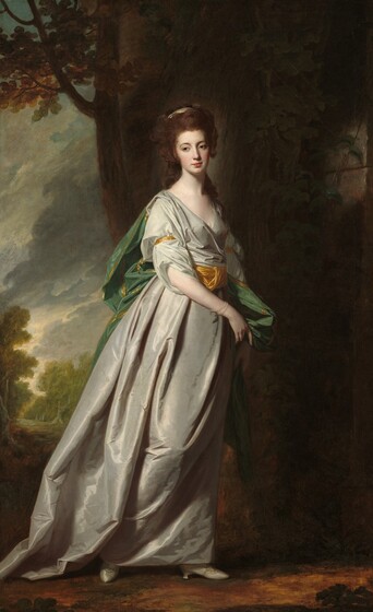 A young woman with smooth, pale skin wearing a fog-gray gown stands in shadowy outdoor setting in this vertical portrait painting. Her body faces our right almost in profile. Her head turns toward us though she looks off to our left with brown eyes under arched brows. Auburn-brown hair frames her heart-shaped face, which has a slender nose over closed, coral-red lips and a dimpled chin. Her long, curly hair is gathered at the back of her head and tied with a sand-brown ribbon. Long tendrils hang down her shoulders and back. Her iridescent gown has a deep neckline and a wide, harvest-gold sash around her waist with matching bands on the upper arms. A shimmering, laurel-green cape bordered in gold falls from her shoulders in deep folds down her back. The woman has pulled some of the cape forward with both hands to hang down her left side, farther from us. She wears delicate, translucent pearl bracelets on one wrist, and steps forward on silvery-gray shoes under the dress’s long hem. Bright light falls across the scene from the upper left so much of the background is in shadow. A stone wall behind the woman spans the right half of the painting. A tree grows up along its leftmost edge, just beyond the woman’s shoulders. A landscape along the left third of the composition opens onto trees under a sky filled with thick, off-white and steel-gray clouds.
