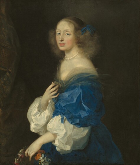 Shown from the hips up, a woman with pale skin, wearing a sapphire-blue gown, looks over her left shoulder at us in this vertical portrait painting. Her body faces our left in profile, and she looks at us from the corners of her large, hooded, gray eyes. She has an oval face with a straight nose, rosy cheeks, and her full, pink lips are closed. Wisps of brown hair fall across her forehead, and her face and neck are framed by a cloud of soft curls tied with a royal-blue bow over the ear on the side we can see. Around her neck is a cream-white pearl choker necklace. Her low-cut bodice is lined with transparent parchment-white fabric, which she holds at her chest with her right hand, farther from us. We see one blousy sleeve of her blue, satin dress, and the sleeve is tied at the elbow. Equally blousy white sleeves cover her forearms. With her left hand, closer to us, she holds a wreath of orange, pale blue, deep pink, and white flowers down by her waist. She is lit from the upper left, and the background behind her is dark in shadow. A patterned curtain hangs along the left edge of the painting.