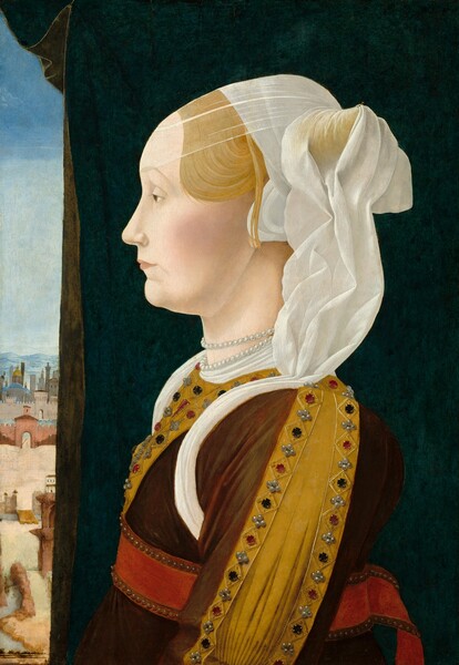 Shown from the waist up, a pale-skinned woman wearing a jeweled dress faces our left in profile in this vertical portrait painting. She looks into the distance with the light brown eye we can see, under a faint, arched brow. She has a petite nose, smooth, lightly flushed cheeks, and her peach-colored lips are closed. Her rust-brown gown is trimmed with wide, mustard-yellow panels studded with pearls, rubies, and sapphires along the front of the bodice and down the sleeve we can see. The elbow of that sleeve, near the bottom edge of the painting, is gathered in intricate, narrow pleats. White fabric billows out from the seam where the sleeve meets her shoulder, and a wide scarlet-red belt bordered with pearls wraps around her waist. Her blond hair is pulled back and coiled into a horn over her ear. Her head is covered with a translucent white veil that falls in deep folds to her shoulder. Another sheer veil layered over the first sweeps down over the high hairline of her forehead. A double strand of white pearls encircles her neck above the white collar of her gown. A marine-blue cloth with an olive-green lining nearly fills the background beyond her, but a sliver of a landscape view can be seen along the left edge of the composition. The window opens onto a town with coral-red city walls in front of blue and gray buildings. Hazy blue mountains line the horizon in the deep distance, and the sky above deepens from pale, ice blue over the mountains to topaz blue across the top.