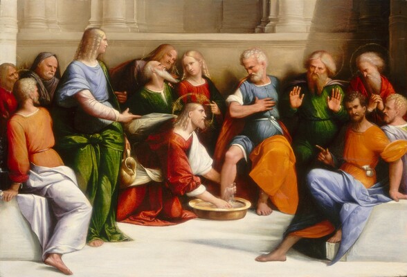 Twelve people are gathered along a stone bench as a thirteenth, kneeling person washes the foot of a man seated in the center of the group in this horizontal painting. All the people have pale skin and wear togas and robes in ruby red, parakeet green, sky blue, pale lilac purple, or pumpkin orange. A faint gold halo encircles each head except for one person, near the lower right. At the center of the painting, the kneeling person, Jesus, faces our right in profile. He has blond, shoulder-length ringlets and a pointed beard. He wears a red, gold-trimmed robe over a white garment. He holds the lower leg of a seated man at the center of the group, and washes the foot in a gold-colored basin. That seated man looks down at Jesus, one hand flat against his own chest. He has short, curly white hair and a full beard. Other people sit and stand along the bench, which spans the width of the composition. Most have beards and look toward Jesus. One is cleanshaven and stands near the left edge of the painting. Another cleanshaven person sits just behind Jesus. A sheer veil is tucked into the squared neckline of that person’s garment, and the front is vertically pleated. The man without the halo sits near the lower right corner, and he looks at us as he points toward Jesus. He has a brown beard and short hair, and a pouch is tucked into the band tied around his orange robe. The floor in front of the group is cream white, as is the bench, which curves in a shallow U shape in front of us. A parchment-white stone building rises immediately behind the group, with columns rising off the top edge.