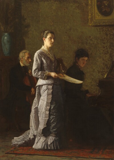 A woman with dark hair pulled up in a bun, wearing a long, muted lilac-purple silk dress, stands singing in front of woman playing a piano and a man playing a cello in a dimly lit room in this vertical painting. All the people have pale skin. Light falls from our left onto the singing woman and the musicians sit in shadow behind her. The singing woman’s body is angled to our right, almost in profile, and she looks up and off into the distance with the light illuminating the curve of her forehead and right cheek. She has dark eyes, an oval face, and her lips are parted. She holds a sheet of paper, presumably music, down at her waist. Her pale purple dress is edged with lace at the neck and cuffs. A ruffle runs down the side of her floor-length skirt, and a ruffle lines the bottom hem around her feet. A train affixed to the back of the dress rests on the floor behind her. Both musicians face our right in profile. To our left, the man playing the cello has a white beard and hair, and he wears a dark suit and glasses. To our right, the woman at the piano wears a dark dress, and her dark hair is pulled up. The singing woman stands on a brick-red, patterned area rug, and the wall behind her is papered with sunflowers loosely sapced against a mottled, gold and caramel-brown background. A tall, light blue vase sits on a mantlepiece along the left edge, next to the cello player. A gold-framed picture hangs on the wall over the pianist.