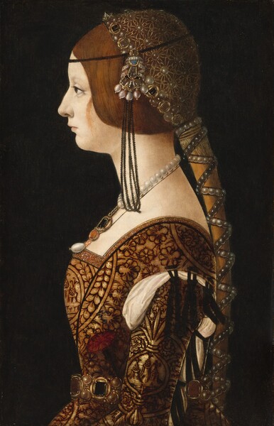 Shown from the waist up, a young, pale-skinned woman faces our left in profile, filling the height of this vertical portrait painting. She is brightly lit from the left and set against an inky black background. A faint eyebrow arches over the green eye we can see, and her blush pink lips are closed. Her auburn-red hair is pulled back with a few loose strands brushing her pale cheek. A cluster of jewels, like a brooch, is affixed to a thin, black band that encircles her brow, over her ear. The brooch has an azure-blue jewel over a knot of four topaz-brown gems, all set in gold. Four pink pearls hang from the bottom edge, and a banner with the words “MERITO ET TEMPORE” intertwines among the jewels along the top. Long, black loops hang from the headband to brush the woman’s shoulder. The headband wraps over an elaborate headdress that covers the back of her head like a cap. The headdress is a golden net adorned with pearls, garnets, and other gems. A thick ponytail falls down her back past her waist, and is wrapped with crisscrossing strands of black and white pearls. Her dress has a low-cut, square neckline, a tight-fitting bodice, and a flaring skirt. The fabric is patterned with stylized flowers and leaves outlined in brown against honey gold. A strand of gleaming white pearls hangs around her thin, long neck over a gold chain with a pendant made up of black and ruby-red gems. One more teardrop-shaped pearl hangs from the bottom of the pendant. A gem-studded, gold belt wraps around her waist. A red carnation is tucked into the belt near her elbow. The sleeve we can see is tied onto the bodice at the shoulder with black cord over cream-white fabric, which cascades out from the wide seams across the shoulder and down the back of the arm.