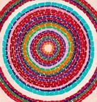 This nearly square, abstract painting is filled with circles within circles, like nested rings, each of a single bright color against the ivory color of the canvas. Each ring is made up of a series of short, rectangular strokes and some bands are narrower while others are a bit wider. The majority of the rings are crimson and brick reds, and they’re interspersed with several bands of lapis blue, two army green rings, and two pale pink rings. The single pumpkin orange band is the smallest, innermost ring at the center. There is one aqua colored ring just inside the lone white ring, which is the first to get cut by the edges of the canvas. A few red, green, and blue rings beyond the white band are only seen at the corners of the canvas. 