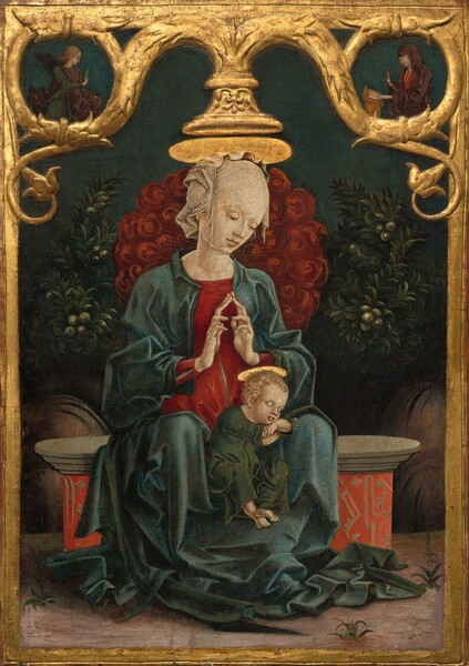 A woman sits facing us on a stone bench with her hands in prayer over the head of a baby who sleeps, propped up between the woman’s knees in this vertical painting. The wood panel on which this is painted is framed by carved, curling gold vines encircling two small people in the upper corners. All the people have pale skin, and plate-like, shiny gold halos seem to rest atop the woman and child’s heads. The woman tilts her head to her left, our right, to look toward the baby with lowered eyes. Her skin is smooth and a translucent white cloth covers her head. She wears a cherry-red dress under a teal-blue cloak that falls in folds over her arms and legs, and pools around her shins and feet. She steeples her elongated fingers to touch in front of her chest. The baby wears a forest-green robe and has bare feet. He props his chin on crossed forearms, which rest on the woman’s left leg, to our right. He has blond, curly hair and delicate features. The woman sits on a stone bench with a base decorated with tan designs against a vivid orange background. Tufts of grass grow in a few areas near her feet and the bench in the dirt ground. A cloud of crimson-red, swirling forms, perhaps blossoms, behind the woman is flanked to each side by leafy, dark green bushes bearing green, round fruit. In a roundel made by the scrolling gold vine in the upper left is occupied by a winged angel facing our right in profile. The angel wears a plum-purple robe over a pine-green garment, and holds up the first two fingers of one hand, palm facing out. In the roundel in top right corner, a woman wearing a dark purple robe covering her head and body over a ruby-red dress sits facing our left in profile. She rests one hand on a book on a wooden desk in front of her and the other hand is raised, palm facing out. The background behind the roundels and the pair below is midnight blue.