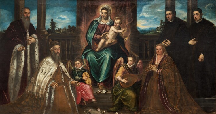 Seven men, women, and children with pale, peachy skin flank a woman surrounded by a halo of light, sitting on a throne and holding a nearly nude baby boy in her lap in this long, horizontal painting. The wide throne sits on a low platform and reaches off the top edge of the canvas. The body of the woman sitting there, Mary, faces us and she turns her head to look down to our left with her lips closed. She wears a loose, dusky rose-pink dress under an aquamarine-blue cloak. A translucent white veil covers her chestnut-brown hair and shoulders, and is tucked into the neckline of her dress. Her right hand, to our left, is raised with the palm down, and she supports the hip and thigh of the baby, Jesus, with her other hand. With his hips facing us, Jesus leans to our right as he twists to hold both hands, palm out, in that direction. He has curly blond hair, and he turns his head back over his shoulder to look down at the people to our left. He has brown eyes under delicately arched brows, flushed cheeks, and his pink lips curve up in a slight smile. Though he appears to be nude at first glance, closer inspection shows he wears a sheer white, short-sleeved, knee-length tunic. Golden rays radiate from Mary and Jesus's bodies and mostly obscure the throne behind them. Two men are shown to our left of the throne and two men and a woman are shown to our right. Mary and Jesus look to our left at an older man with a long, gray beard. He kneels with his body angled to our right with both hands lifted palms down at waist height. He looks at us from the corners of his dark eyes under arched brows. He wears a voluminous, honey-brown robe lined with black spotted, white fur and covered over the shoulders and arms with a white fur cape. His matching brown cap has a pattern around the edge, perhaps beading. Standing behind the kneeling man to our left is a bareheaded man with a long, pointed gray beard and short-cropped, gray hair. He also looks out at us with brown eyes, which are lined at the corners with wrinkles. His robe is burgundy red and also lined with black and white fur down the front and around long, drooping sleeves. To our right of the throne, a woman with blond hair in tight curls kneels with her hands together in prayer at her chest. She looks at us with gray eyes set in a round face. Her full robe is patterned with sage-green vines and leaves against an amber-brown background, and is lined along the sleeves and down the front with maroon red. Behind her and to our right stand two young men with short brown hair, wearing dark brown robes with high, white collars. The man to our left has a thin mustache and the other is cleanshaven, and they both look off to our left. Two winged angels sit on the platform to either side of Mary’s feet, which is strewn with roses. The wings of both angels are painted with golden yellow and rust red. To our left, the child-like angel has short, brown hair and wears a teal-blue jacket with a white ruffle at the neck. Coral-red drapery covers the legs over bare feet, and the angel plays a violin. The angel to our right of Mary’s feet is a little taller, and has curly brown hair. Wearing butter yellow and moss green, that angel strums a lute and looks out at us with dark eyes. To either side of the throne, the room is lined with a balustrade and columns, framing a landscape with rolling green hills and ice-blue mountains. White clouds are streaked across the vivid blue sky.