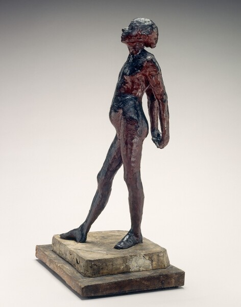 A young, nude girl is roughly modeled with glossy navy blue and wine-red beeswax in this freestanding sculpture. She faces our left in profile in this photograph. Her weight rests on her left foot, closer to us, and her other leg extends long, the foot turned out at an angle. Her hands are clasped behind her back, and her round belly projects from her swayed hips. Her head is tipped back and her eyes closed. She stands on a double pedestal. A crack runs across one corner of the top, white, square plaster pedestal. A wider wood pedestal is below.