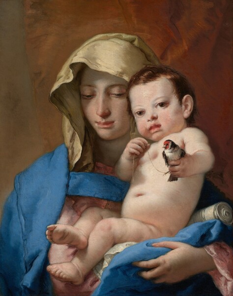 Shown from the chest up, a young woman faces us holding a nude baby in her arms in this vertical painting. They both have pale, peachy skin with pink cheeks. The woman has an oval face with a thin nose, and her coral-pink, bow mouth is closed. She looks down and to our left with dark eyes under arched brows. Her hair is covered by a white veil, and an azure-blue mantle is draped over her rose-pink robe. She cradles the plump child in her crossed arms. The baby has short, wavy, copper-red hair framing a round, flushed face with a button nose, peach lips, and hazel eyes that look at us. He holds a bird in his left hand, on our right. The bird has an off-white body with charcoal-gray wings and neck, and a strawberry-red face. A delicate chain wraps around the bird’s foot, and the baby holds the end in his other hand, up by his chest. A golden brown curtain covers most of the space behind the pair, except for a sliver of stone-gray wall to our left.