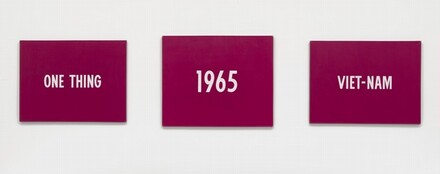 Three horizontal paintings with raspberry-pink backgrounds and white text hang spaced out in a row against a white background. The central panel is slightly larger than those hanging to the sides. The white text on the left panel reads, “ONE THING.” In the center is “1965,” and the panel to our right has, “VIET-NAM.”