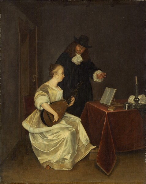 A woman wearing a pale yellow silk dress sits playing a lute in front of a table while a man, wearing a black suit and hat, stands behind her in this vertical painting. Both have light skin. The woman sits facing our right in profile as she looks at pages of sheet music propped on a wooden tabletop stand on the table in front of her. Her light brown hair is pulled back in a braid looped into a bun, and a few curly tendrils fall alongside her ears. She has a pointed nose, full cheeks, and a receding chin beneath closed lips. Light gleams off her pale, golden yellow jacket and skirt. The jacket has elbow-length sleeves and is lined with white fur, and her long skirt has a band of deep gold embroidery and possibly beading down the front and along the bottom hem. She rests one foot on a low wooden box, and the other is covered by her skirt. She sits in a straight-backed chair with a wine-red, upholstered back. The table in front of her, to our right, is covered with a burgundy-red cloth. Near the music stand are a small book with a brown cover, a silver, oval-shaped box, a silver candlestick holding a white, unlit candle, and a bunched up white cloth. Behind her, the man stands with his left hand, on our right, lifted over the sheet music. He tips his head forward to look down at the woman or her lute. He has thick, shoulder-length, wavy brown hair and a goatee. He wears a tall, brimmed, black hat, and there are ruffles of white fabric at his neck and the cuffs of his long sleeves. The room has a brown floor and smoke-gray walls. A door opens a little into the room to our left, behind the pair.