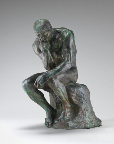 This free-standing bronze sculpture shows a nude, muscular man sitting on a rock and resting his chin on the back of his right hand, with that elbow propped on his left knee. In this photograph, the man’s body is angled slightly to our left. He hunches a bit as his body twists so his right elbow, on our left, reaches the opposite knee. His other rests along his leg so the hand dangles beyond the knee. The man has short-cropped hair, a furrowed brow, an angular nose, and lines around his mouth and eyes. The foot on our right rests higher on the rock so that knee juts up a little higher than the other. The bronze has a greenish patina, especially noticeable along the top of the man’s head and shoulders and the front of his lower legs.