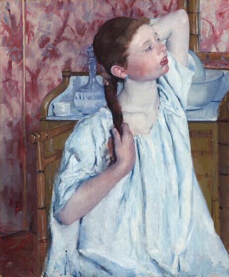 We look slightly down onto a round faced girl with flushed, pale skin sitting almost in profile on a ladderback chair, facing our right. Shown from the lap up, she almost takes up the height of this vertical painting. She wears a voluminous, ice-blue chemise with elbow-length sleeves and a round, sapphire-blue earring in the ear we can see. Her head is tilted slightly back as she reaches up with both hands. With her right hand, closer to us, she holds the end of a chestnut-brown braid hanging over that shoulder. Her other elbow points upward as she touches hair at the base of the neck. Her lips and face are deeply flushed in her otherwise pale face. Her mouth hangs slightly open, revealing white teeth as her half-closed violet-colored eyes gaze off to our right. She sits in the corner of a room with wallpaper decorated in a pattern of tree limbs and leaves in cranberry red and slate blue on a mauve-pink background. A peanut-brown dresser behind her is covered with a white cloth on which sit a white cup and glass pitcher with a tapered neck. A white porcelain ewer and washbasin, tinged with blue, are partially visible behind her bent left elbow. The lower corner of a mirror in a bamboo frame hangs from the upper right. A portion of a burgundy rug fills the lower left corner.