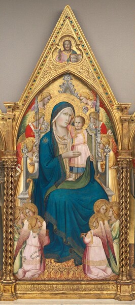 A woman sitting on a throne supports a baby as twelve winged angels look on, all framed in a carved, gilded pointed arch in this vertical panel. It is the center of a three-panel triptych. The background behind all the people is gold, and the top of the panel comes to a rounded, pointed arch under a second taller, sharper point. Trios of spiraling columns frame the left and right sides. The woman, child, and angels all have pale skin tinged faintly with green, and rosy cheeks. They all have blond hair except for the woman, whose hair is covered, and all have plate-like gold halos that overlap, sometimes obscuring the bodies of others. The woman, Mary, faces us from her ivory-white, carved stone throne. She looks slightly above us with brown eyes under delicate brows. She has a small, straight nose, and her narrow pink lips are closed. The lapis-blue robe that covers her head and body is bordered with gold patterns, and has a starburst on her right shoulder, to our left. The pea-green underside of the mantle is visible where it turns over on the sleeves and down the front, and the robe is worn over an ivory-white dress patterned with gold. The child she holds with both hands, Jesus, stands on her lap and wraps one arm around her neck. His other hand grips the high neckline of her dress. He looks up with dark, close-set eyes. He has curly blond hair, a double chin, and rounded cheeks. Two tiny teeth are barely visible below his pink upper lip. Despite the rounded cheeks, his face looks more like that of an adult, and the proportions of his body are also adult-like. He wears a gold-trimmed, pale pink robe over a blue garment, which stops just short of his bare feet. The twelve angels surrounding the throne are grouped in trios, with three looking on to our upper left, three to our upper right, and then two trios gathered in each lower corner. Their wings and robes are painted in tones of celery green, ruby red, butter yellow, and pale rose pink. Each has a triangular diadem above their foreheads. The floor beneath is patterned with gold against a burgundy-red background. Above Mary and Jesus, a bearded man is shown from the chest up in a shape made of three lobes alternating with three points. That man faces us and holds up his right hand, to our left, with the first two fingers raised. He wears a shell-pink garment under a green robe, and holds up an open book with Latin text with his other hand. The frame around Mary, Jesus, and the gable above is carved and gilded. Barely discernable, the panel is inscribed across the bottom below the throne, “AVE MARIA GRATIA PNELA DOMINUS.” The pages of the books read, “EGO SUM A O PRINCI PIU FINIS EGO SUM VI A. VERITAS VITA.”