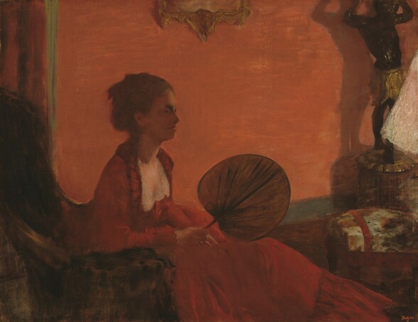 Dominated by tones of red and fire orange, this nearly square painting shows a seated woman leaning forward in a high-backed chair, holding a round, flat, leaf-shaped fan. She sits to our left facing our right in profile, so the back of the chair is cropped by the edge of the composition. The coral red wall behind the woman spans the width of the painting and the skirt of her long ruby-red dress extends almost to the bottom right corner of the canvas. Her brown hair is pulled up and her face is in shadow. The flat disk of the fan rests on its edge on her lap, almost at the center of this painting. A few objects cropped by the right edge of the painting break up the suffused red palette, including a black sculpture of a person with arms raised overhead, a footstool, and a triangular white form, perhaps a lamp shade.