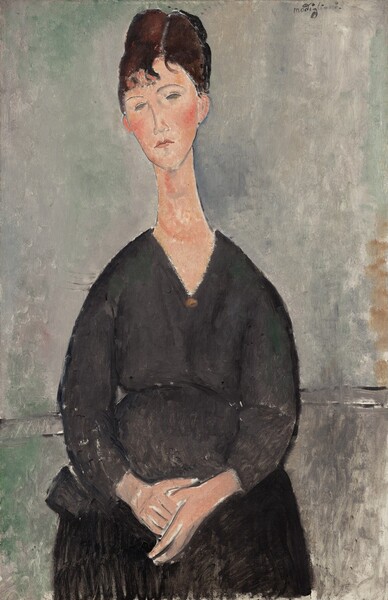 Shown from the knees up, a woman wearing a black dress is painted with areas of mottled color in this vertical painting. The woman’s body faces us, her shoulders sloping steeply down from her elongated neck. She sits with her hands in her lap, and she looks down and to our left. Her peach-colored, long, narrow face comes to a point at her chin, and her cheeks are flushed pink. Her almond-shaped eyes, curved brows, long nose, and closed lips are outlined with gray. Her brown hair is pulled up and back, and short bangs brush her forehead. A gold-colored disk at the point of the dress’s V-neck could be a brooch. Two parallel black lines suggest a chair rail running behind the woman’s elbows. The background is painted with visible strokes of fog gray and moss green above the rail and darker, elephant gray below. The artist signed the upper right corner, “modigliani.”